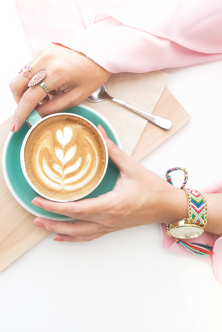 Woman wearing pink sleeves and jewellery holding a coffee