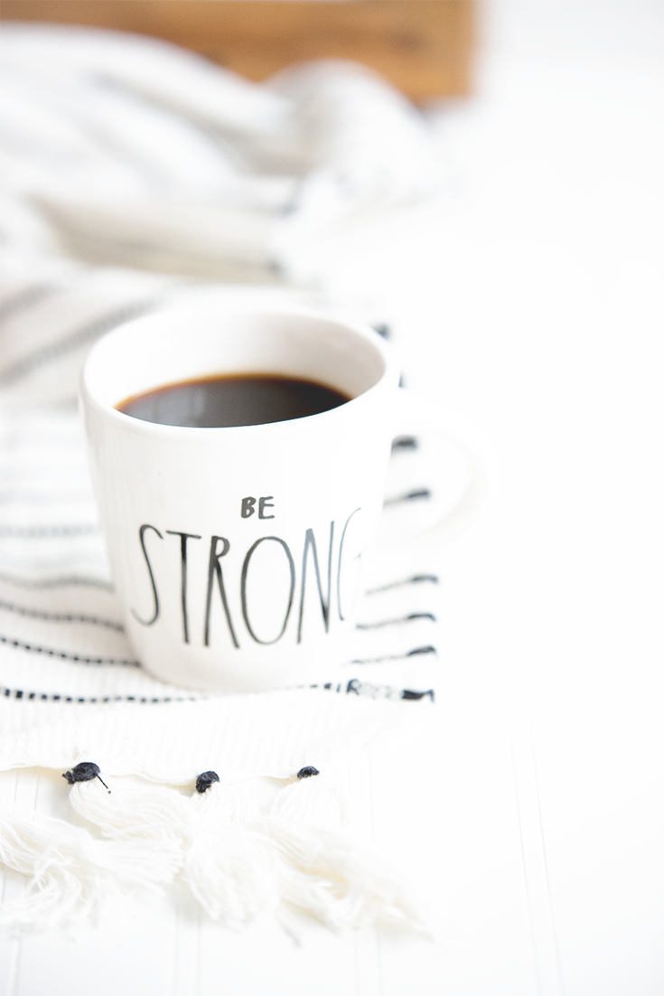 White mug with the words 'be strong' against black and white scarf